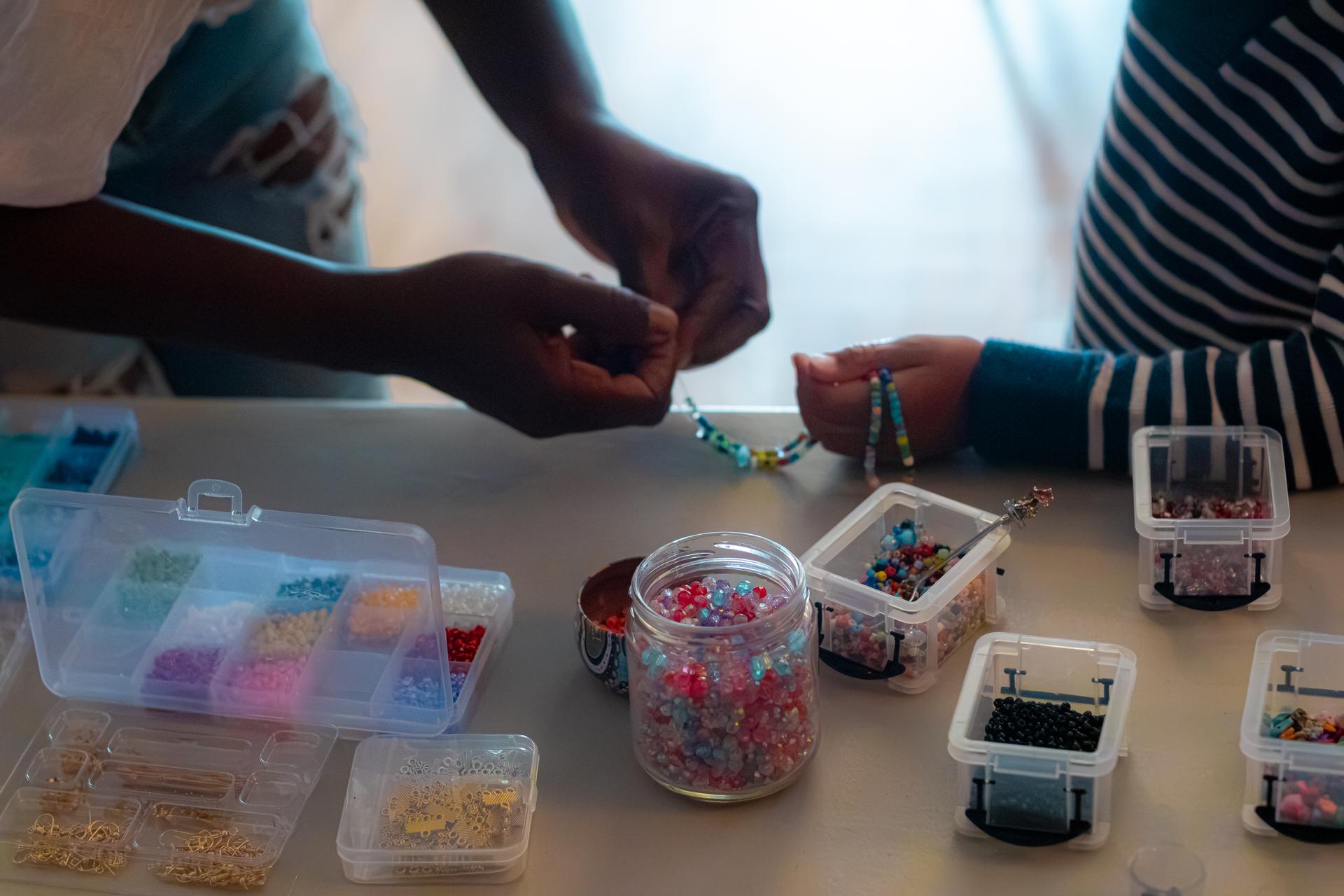 Deux jeunes assemblant leurs bracelets de perles à contre-jour, entourés de boîtes de perles colorées