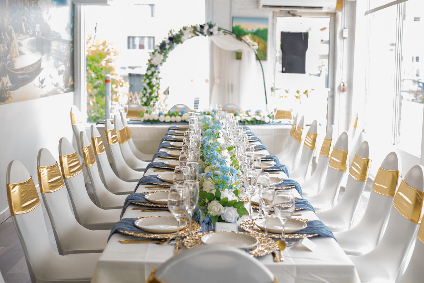 Table de réception habillée de blanc et de fleurs bleues sous une arche florale
